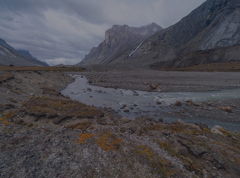 Photographie d'un petit ruisseau entre deux flancs de montagnes rocheuses et un ciel nuageux au Nunavut.