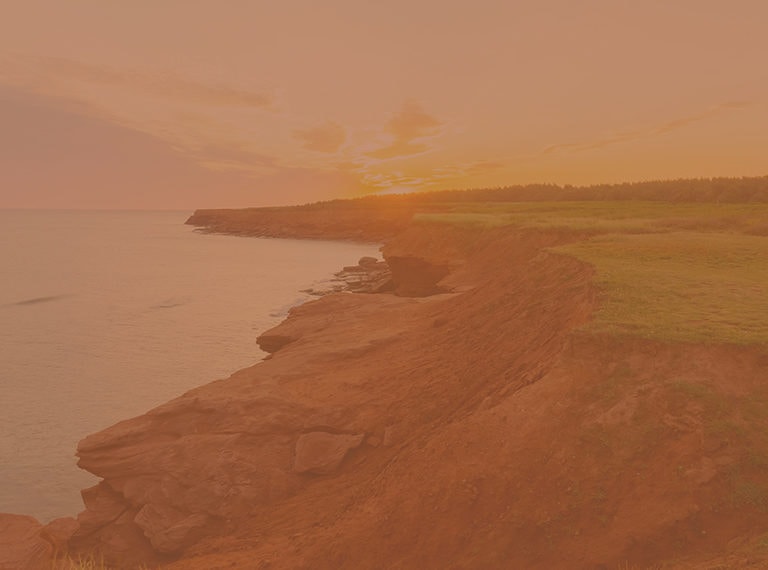 Photographie de la côte de l'Île-du-Prince-Édouard avec une pente sablonneuse jusqu'à l'eau et une herbe verte et plate.